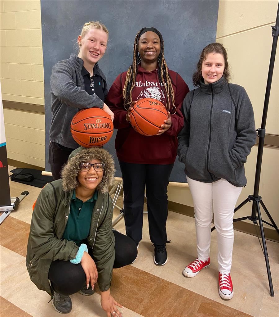Four students posing for the camera. Two hold basketballs and one crouches down.